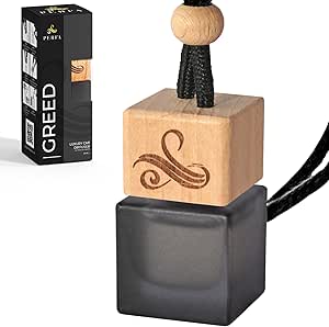 A wooden air freshener with a black base and a box labelled "GREED" in the background.