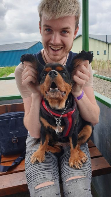 A smiling person holds a happy dog with perked ears, both sitting outdoors.