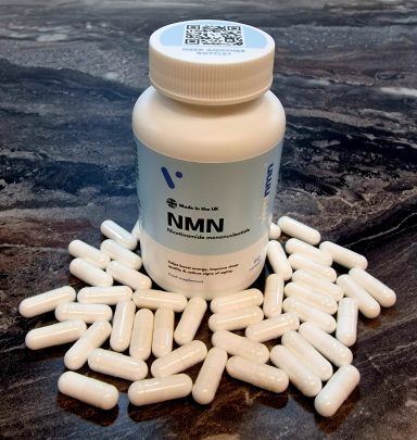 Bottle of NMN dietary supplement surrounded by white capsules on a dark surface.